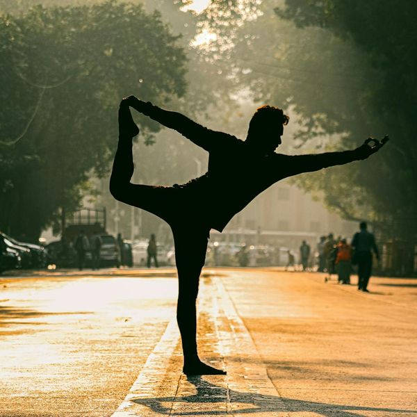 A person balancing in a yoga tree pose against a sunset.
